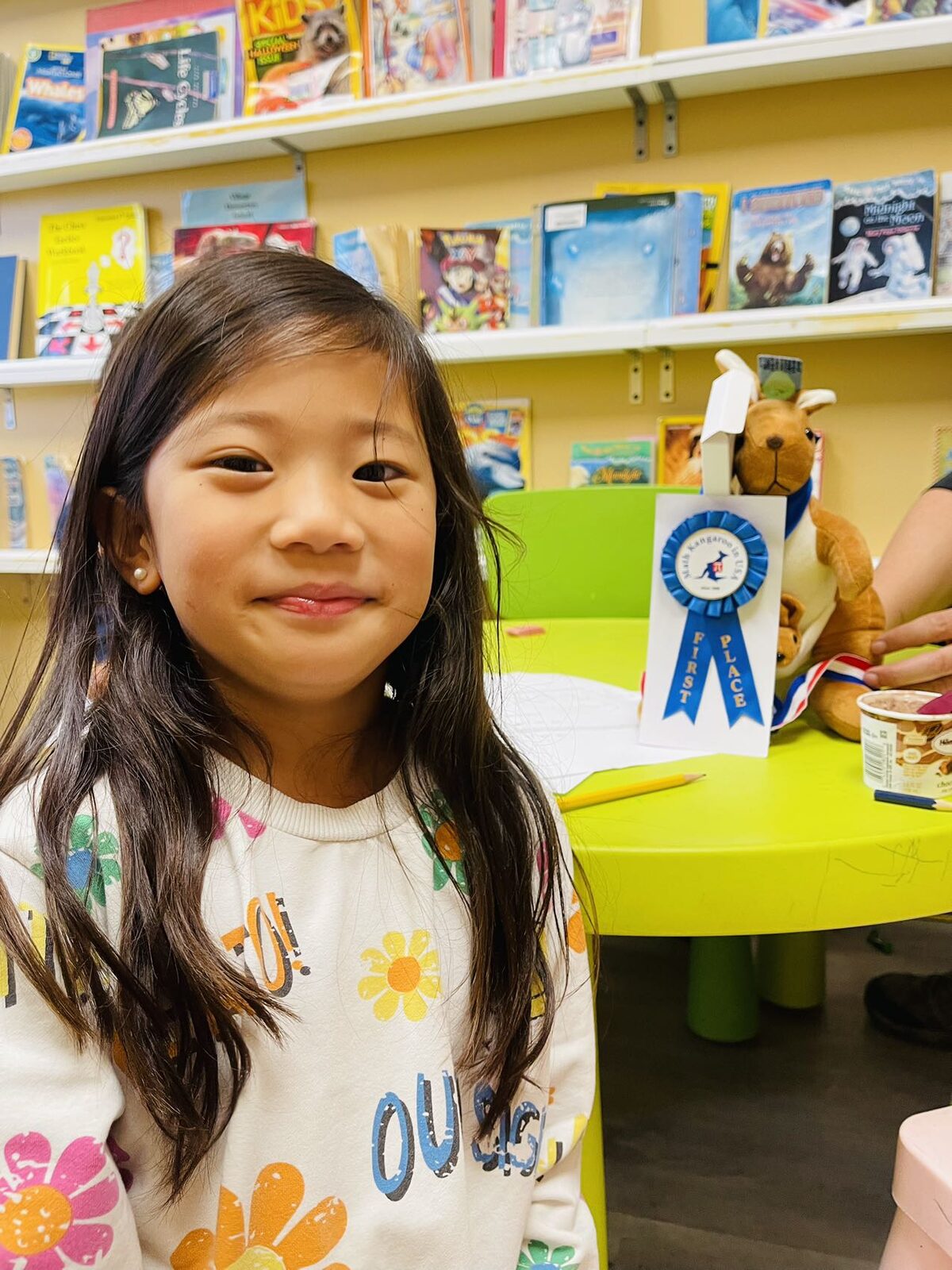 Smiling student with her First Place ribbon and the Math Kangaroo mascot